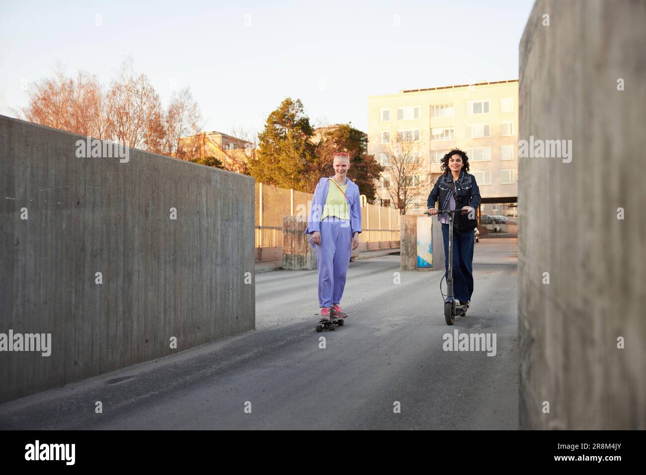 Junge Frauen beim Skateboarden und Motorroller fahren Stockfoto