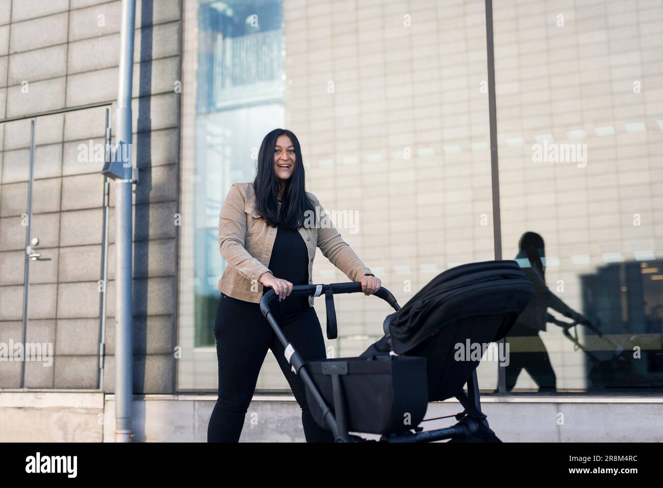 Blick auf eine lächelnde Erwachsene Frau im Elternurlaub, die einen Kinderwagen schiebt Stockfoto