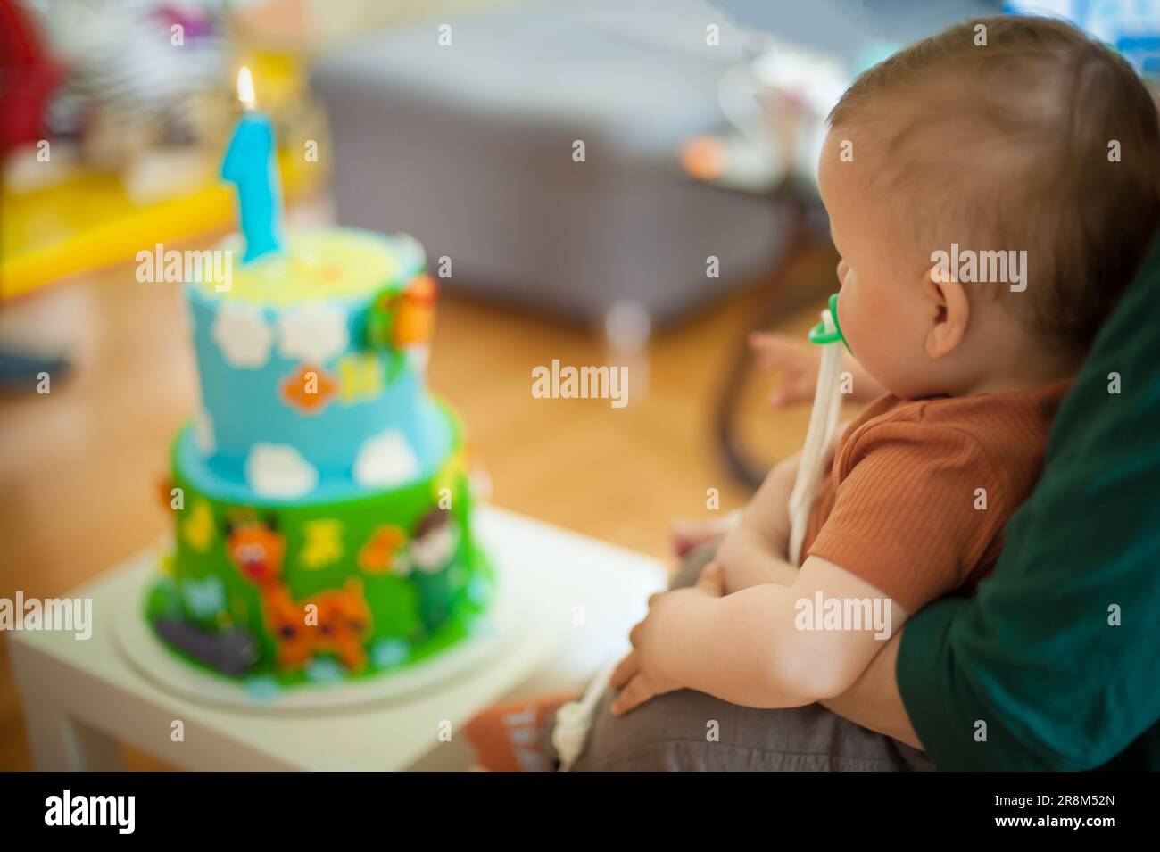 Der süße kleine Junge feiert seinen ersten Geburtstag mit seiner Familie zu Hause. Kuchen und Kerze in Form von Nummer Eins Stockfoto