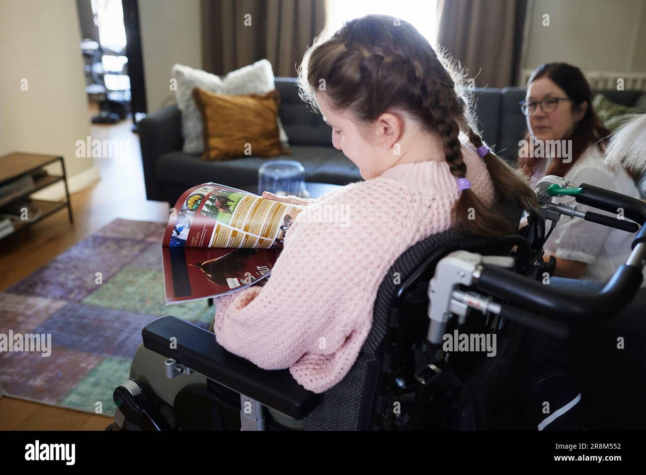 Behindertes Mädchen im Wohnzimmer liest Zeitschrift Stockfoto