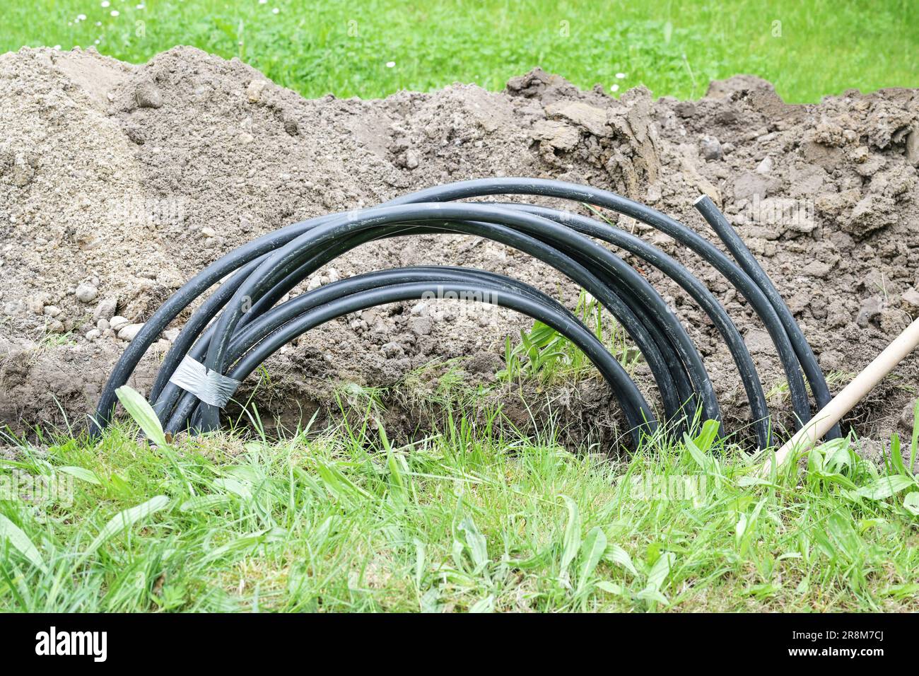 Schwarzes Spiralkabel in einem schmalen Graben im Rasen, um einen Hausanschluss zu installieren, Energiekonzept, Kopierraum, ausgewählter Fokus Stockfoto