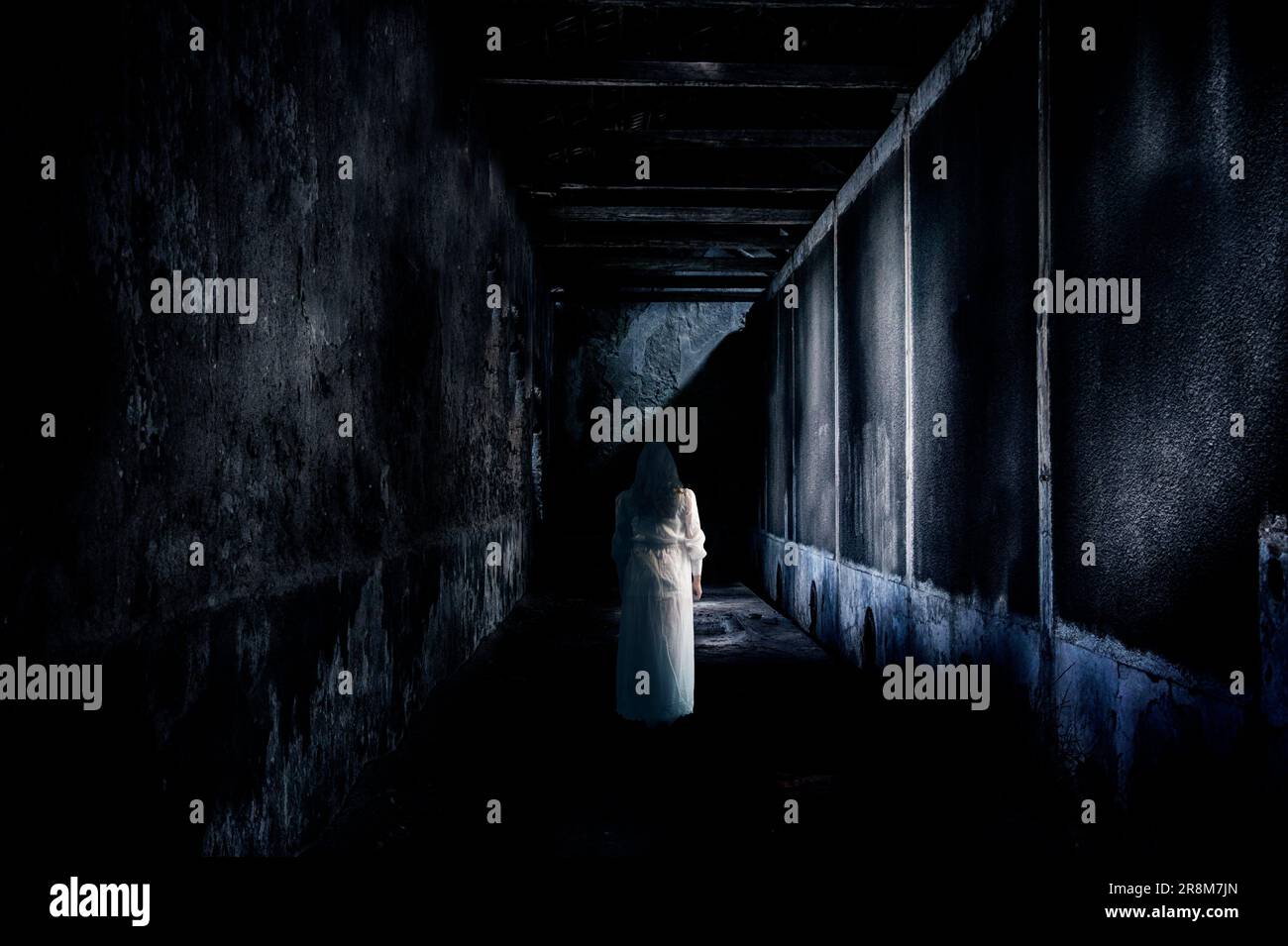 Eine Frau in einem weißen Bademantel, die in einem dunklen, geheimnisvollen, verlassenen Gebäude spaziert Stockfoto