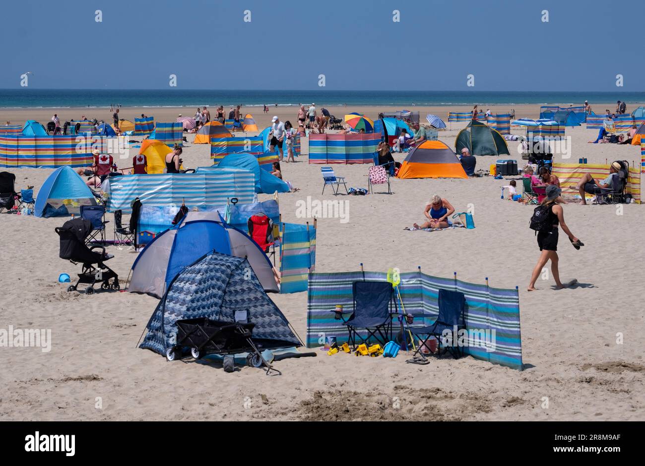 Urlauber genießen den Sonnenschein am Strand von Peranporth, Cornwall, England. Mehrfarbige Windunterbrechungen und Regenschirme bieten Schutz vor der Hitze. Stockfoto