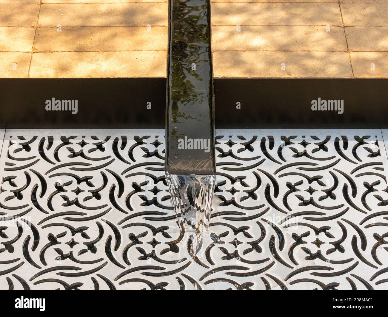 Nahaufnahme eines Gartenrills aus Metall, der in einen mit einem lasergeschnittenen Gitter bedeckten Pool in einem britischen Ausstellungsgarten fließt. Stockfoto
