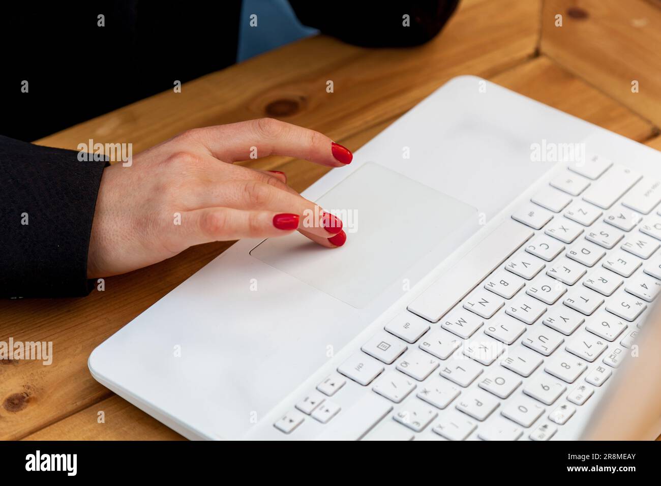 Weibliche Hände mit roter Maniküre auf dem Hintergrund eines weißen Laptops. Das Mädchen im Café arbeitet an einem Laptop. Stockfoto