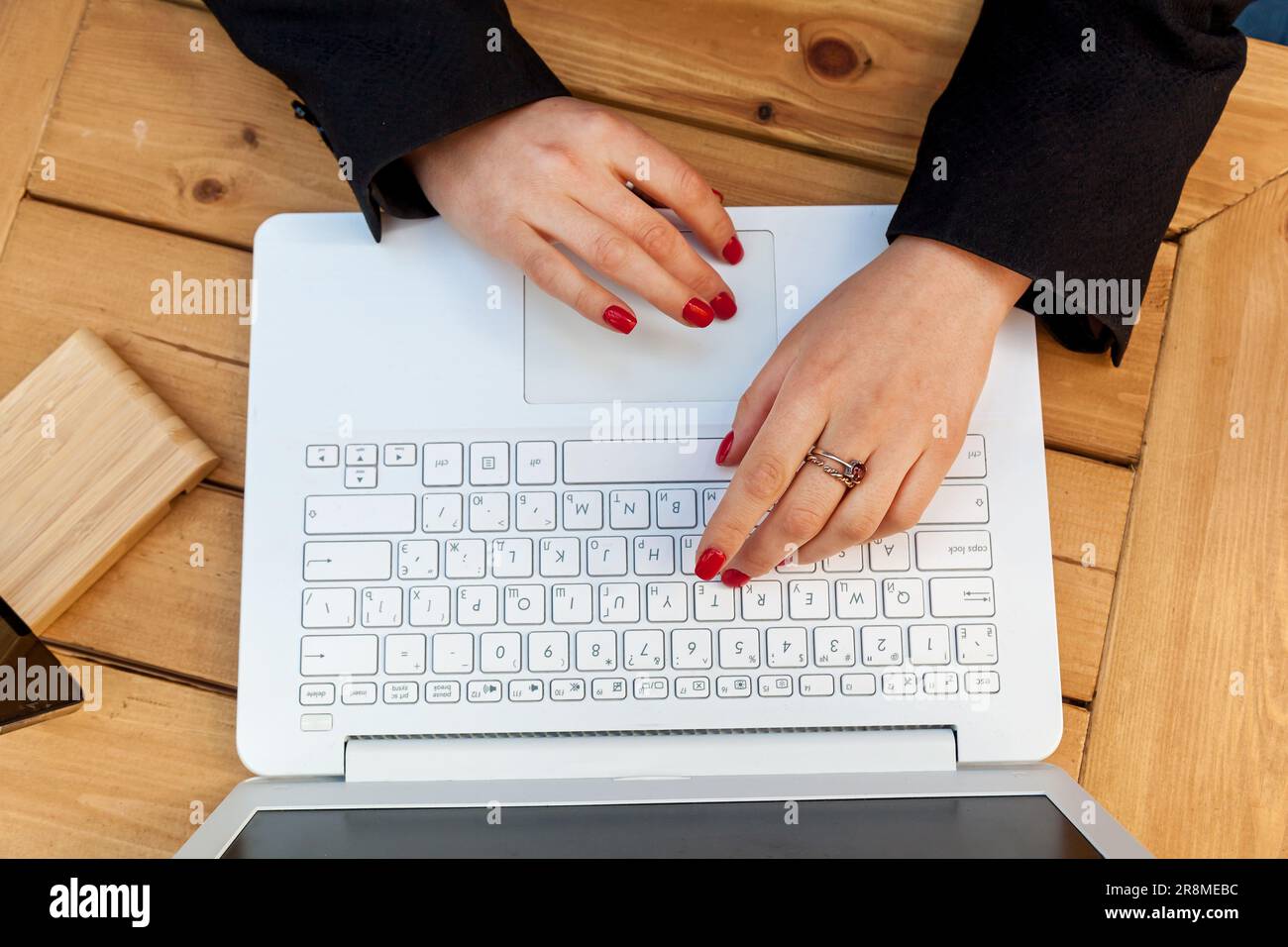 Weibliche Hände mit roter Maniküre auf dem Hintergrund eines weißen Laptops. Das Mädchen im Café arbeitet an einem Laptop. Stockfoto