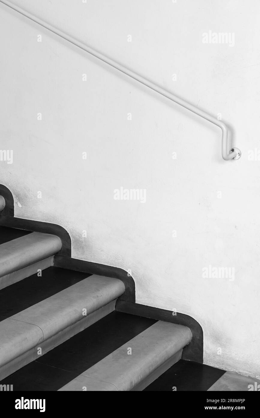 Treppe und Handlauf an einer weißen Wand, abstraktes vertikales Hintergrundfoto, schwarz-weiß Stockfoto