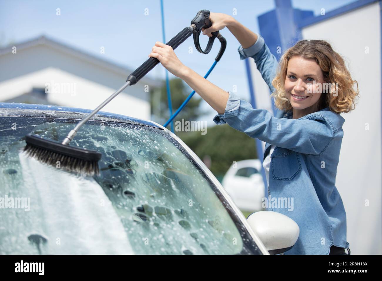 Frau wäscht Auto mit Schlauch- und Bürstenaufsatz Stockfoto