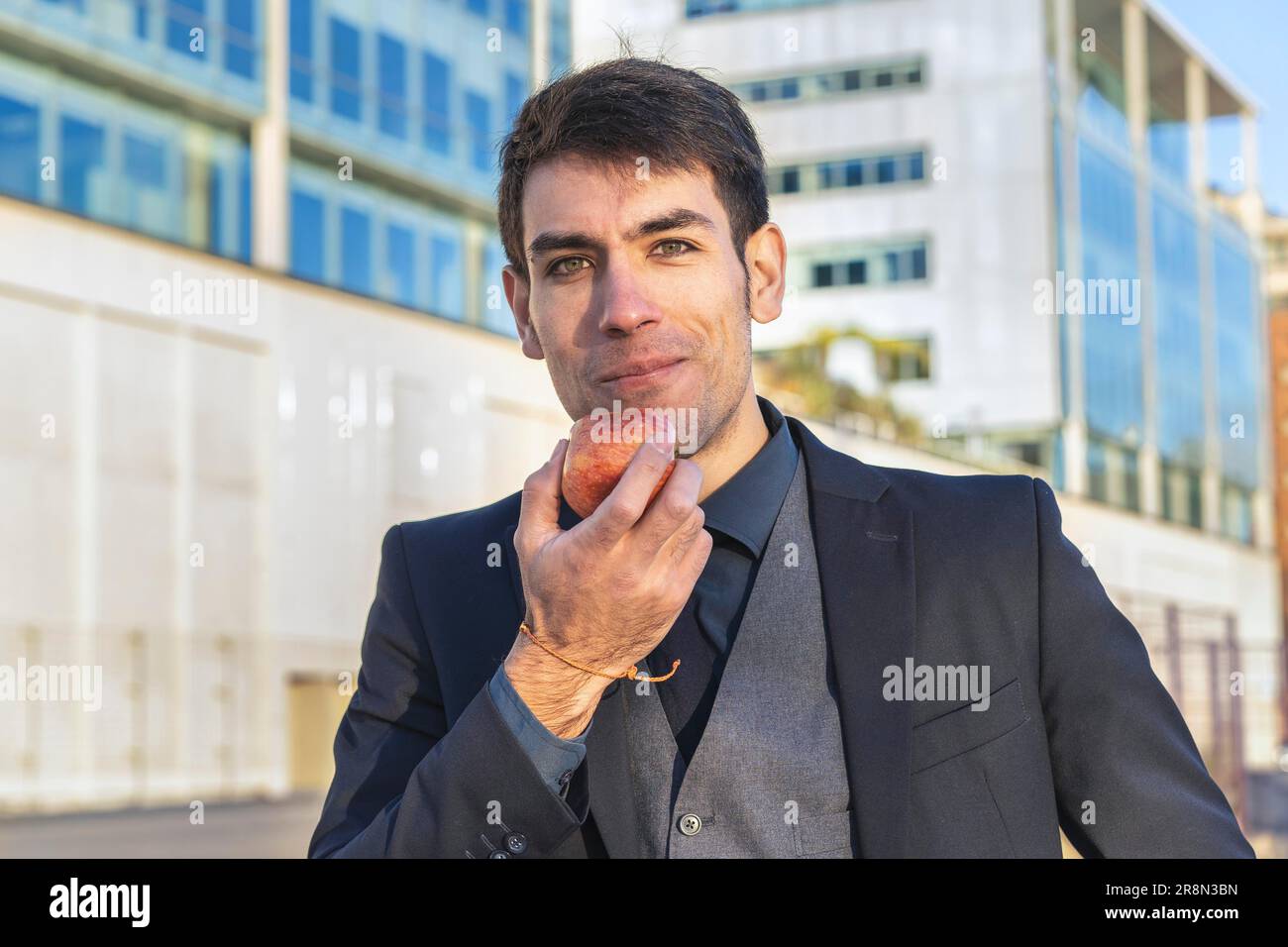 Ein attraktiver Geschäftsmann, der auf der Straße in der Nähe seines Büros einen Apfel essen will Stockfoto