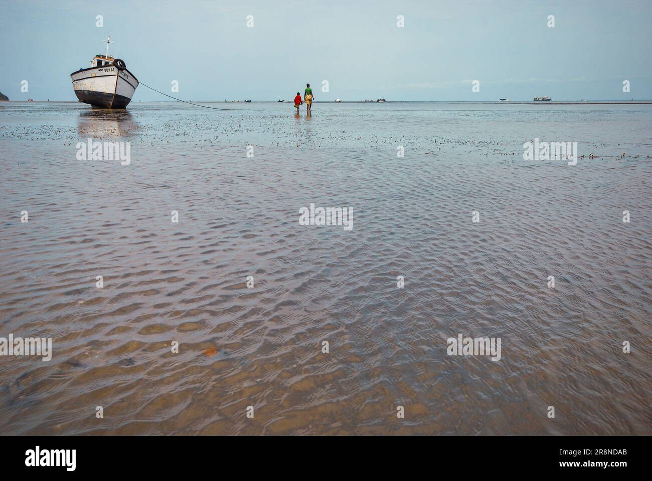 Mutter und Tochter gehen bei Ebbe an einem Fischerboot vorbei, Inhaca Island Mosambik, ca. 2009. Stockfoto