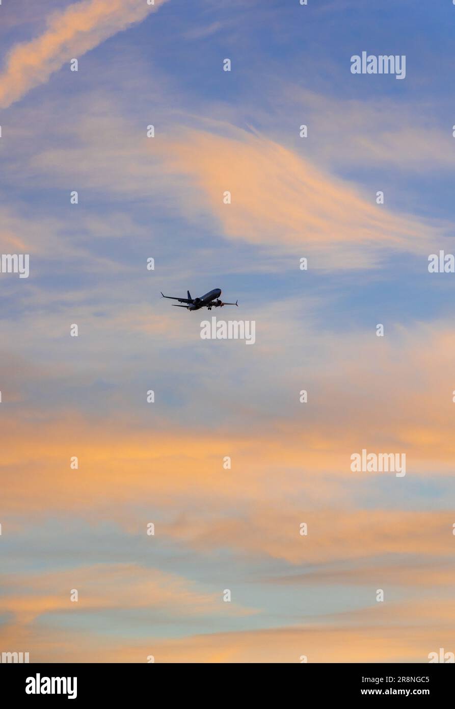 Ein modernes Passagierflugzeug, das bei Sonnenuntergang durch einen pastellfarbenen Himmel fliegt Stockfoto
