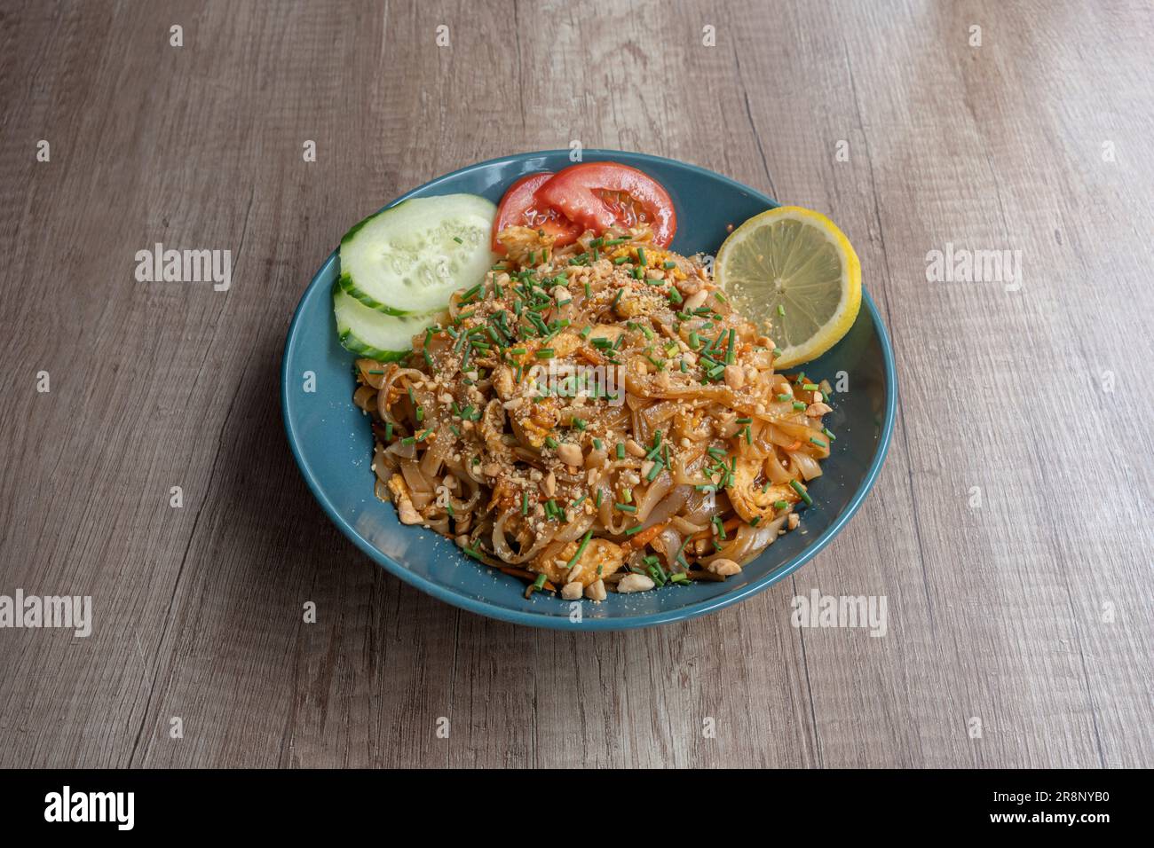 Asiatische Dishe kulinarisches Stillleben. Pad Thai Nudeln mit Huhn, Samen, Tomaten, Gurken und Zitrone Stockfoto