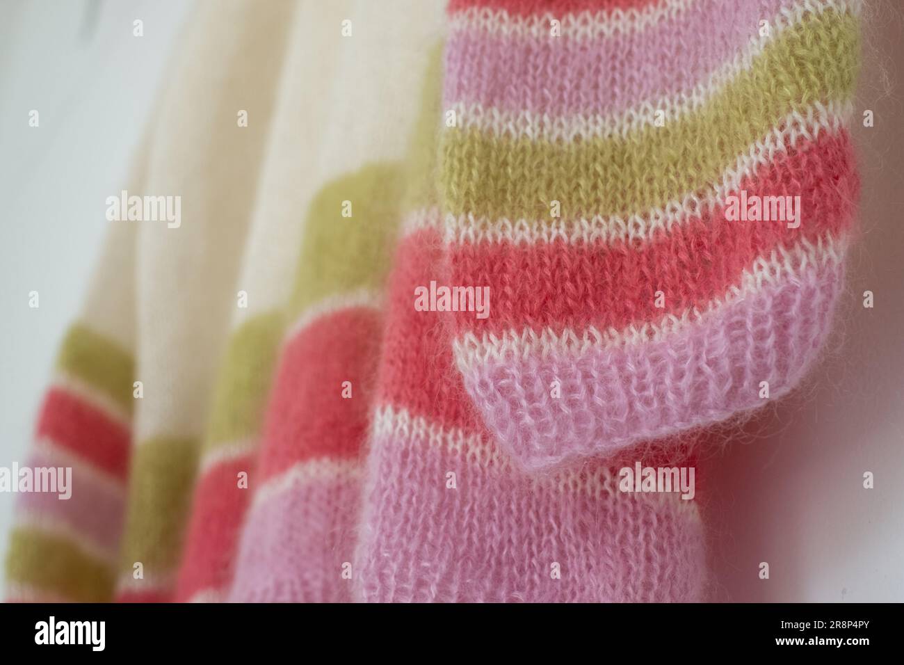 Nahaufnahme eines handgestrickten Pullover aus pinkfarbenem, weißem und grünem Bonbon mit gestreiftem Mohair-Garn und Stickerei mit Strümpfen und Rippen. Stockfoto