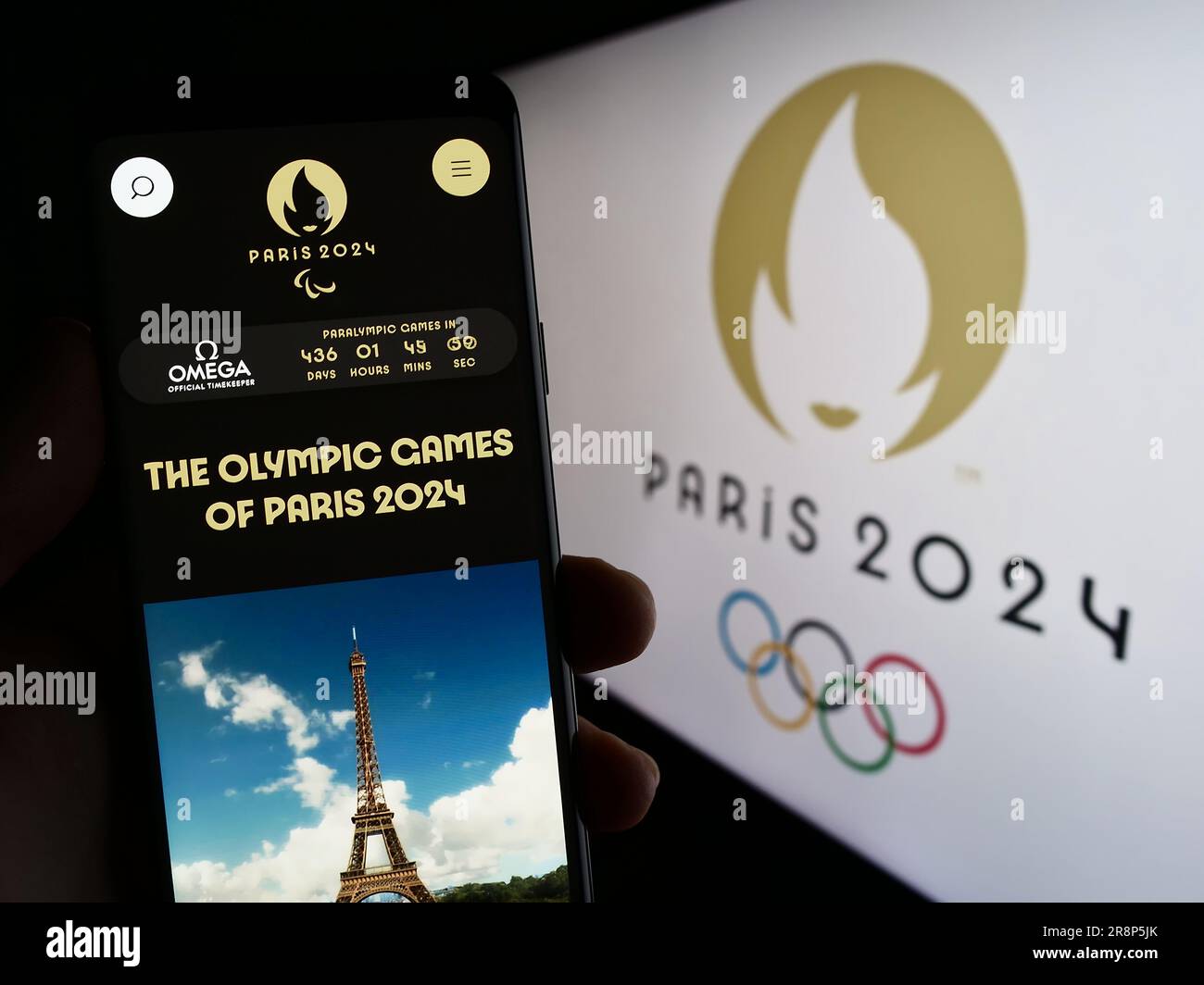 Person mit Smartphone und Website der Olympischen Sommerspiele 2024 in Paris auf dem Bildschirm vor dem Logo. Konzentrieren Sie sich auf die Mitte des Telefondisplays. Stockfoto