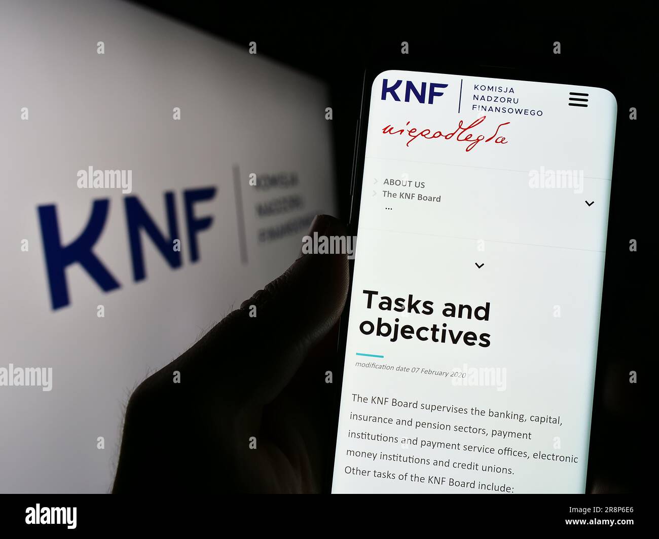 Person, die ein Mobiltelefon mit der Website der Behörde Komisja Nadzoru Finansowego (KNF) auf dem Bildschirm vor dem Logo hält. Konzentrieren Sie sich auf die Mitte des Telefondisplays. Stockfoto