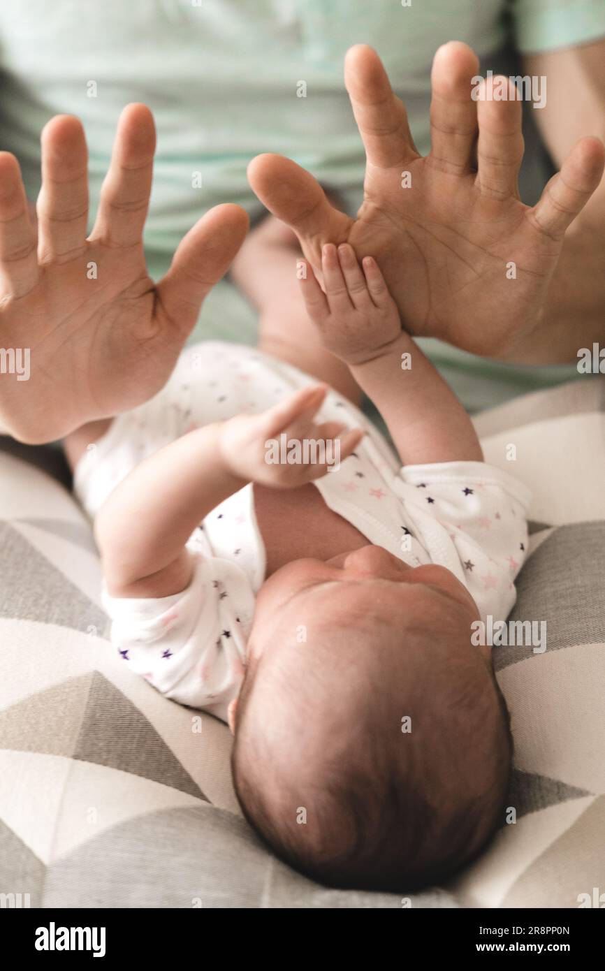 Ein Baby kichert und erforscht spielerisch die Hände seines Vaters, wodurch ein fröhlicher und verbindender Moment zwischen Vater und Kind entsteht. Stockfoto