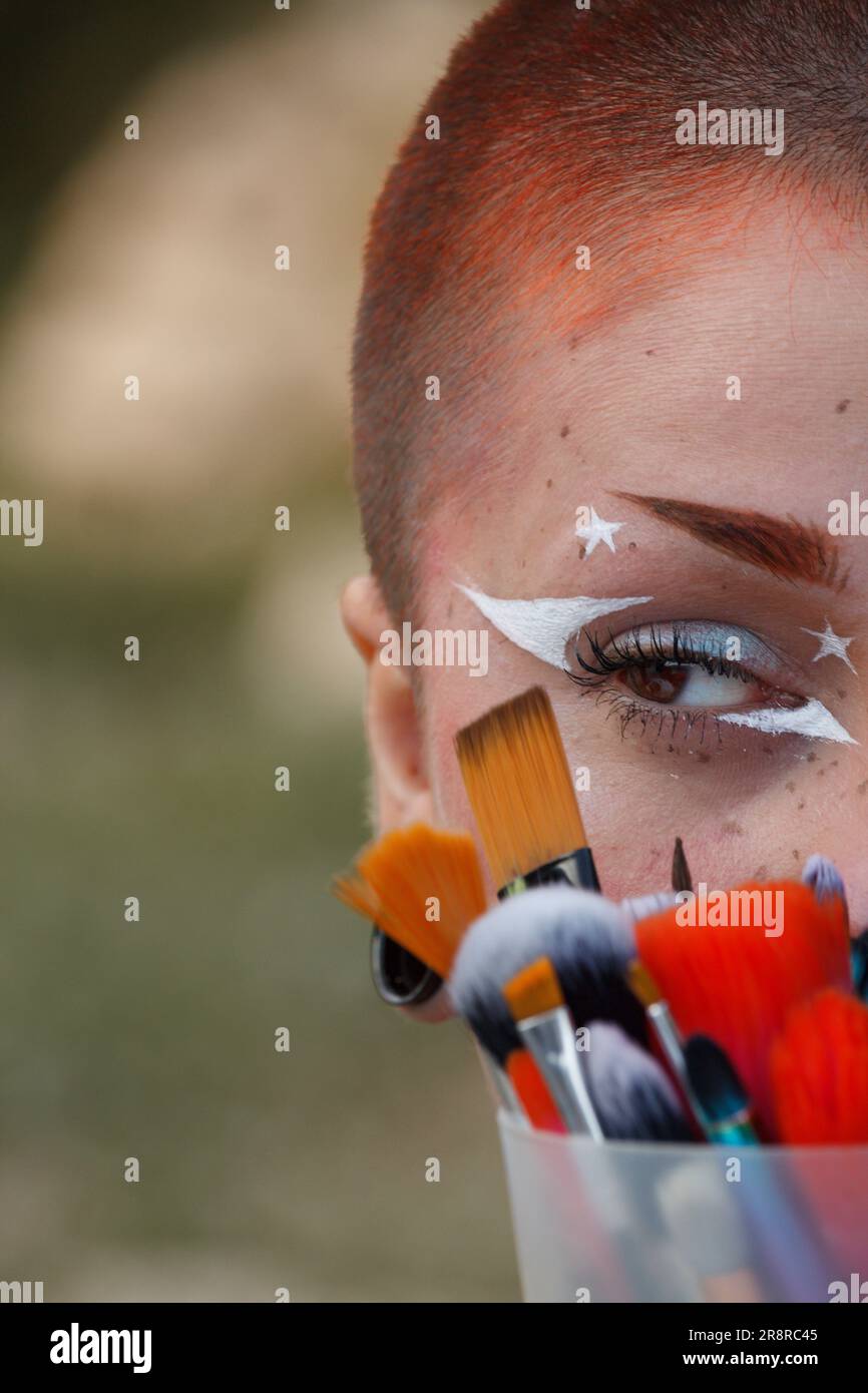 Halbgesichtsporträt einer jungen, schönen Frau mit schickem Make-up und bunten Make-up-Bürsten im Gesicht Stockfoto