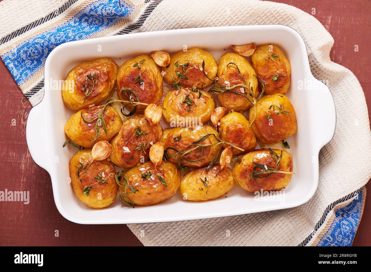 Geröstete Kartoffeln mit Knoblauch, Thymian und Rosmarin in Keramikbackform, Draufsicht Stockfoto