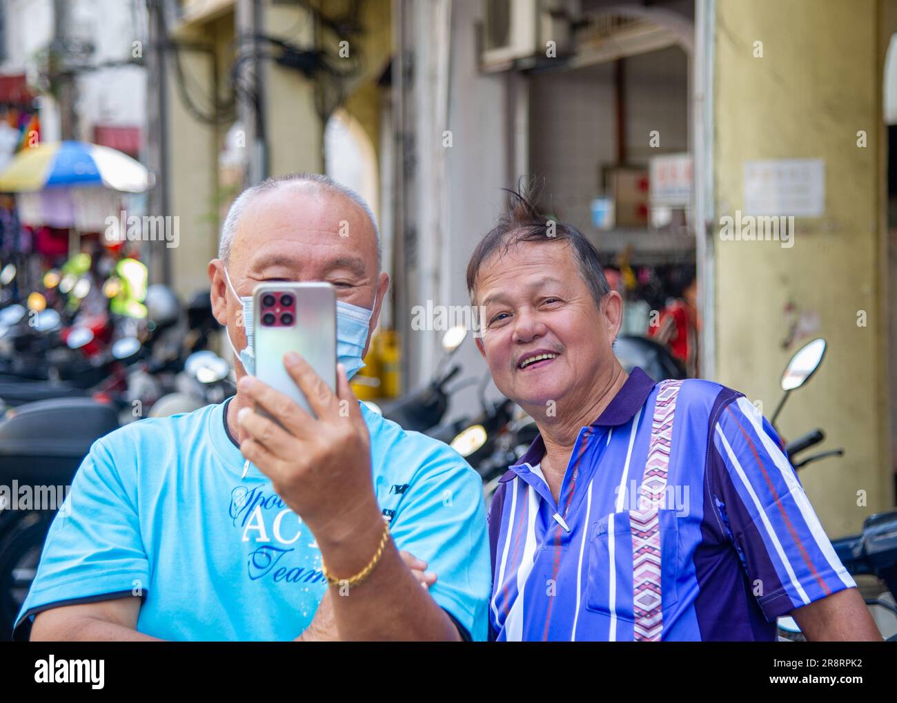 Februar-21-2023- Penang-Malaysia- zwei Männer in GorgeTown fotografieren mit ihren Handys von Touristen auf einem Markt in blauen Hemden Stockfoto
