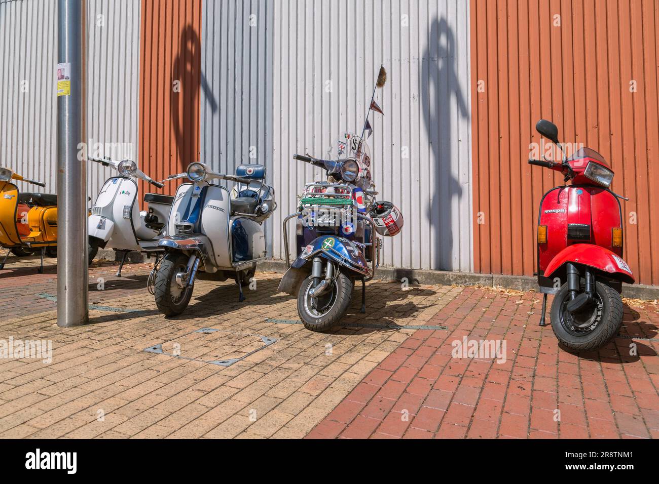 Eine Reihe von Motorrollern, die in einer Straße geparkt sind. Moderner Roller. Vespa und Lambretta haben geparkt. 1960er Popkultur. Stockfoto