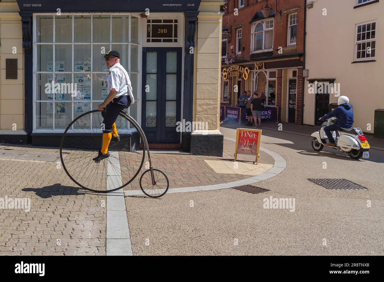 Ein Kontrast von Alt und Neu, wie ein Penny-Far-Fahrrad und ein Motorroller an einer Kreuzung verschiedene Routen nehmen. Eine Person, die einen Penny fährt. Stockfoto