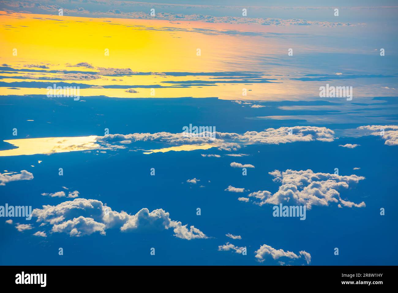 Blick auf die Wolken vom Flugzeugfenster bei Sonnenuntergang über den Wolken. Wolken und Sonne am Himmel. Die Sonne strahlt ein helles gelbes Licht aus, das den beleuchtet Stockfoto