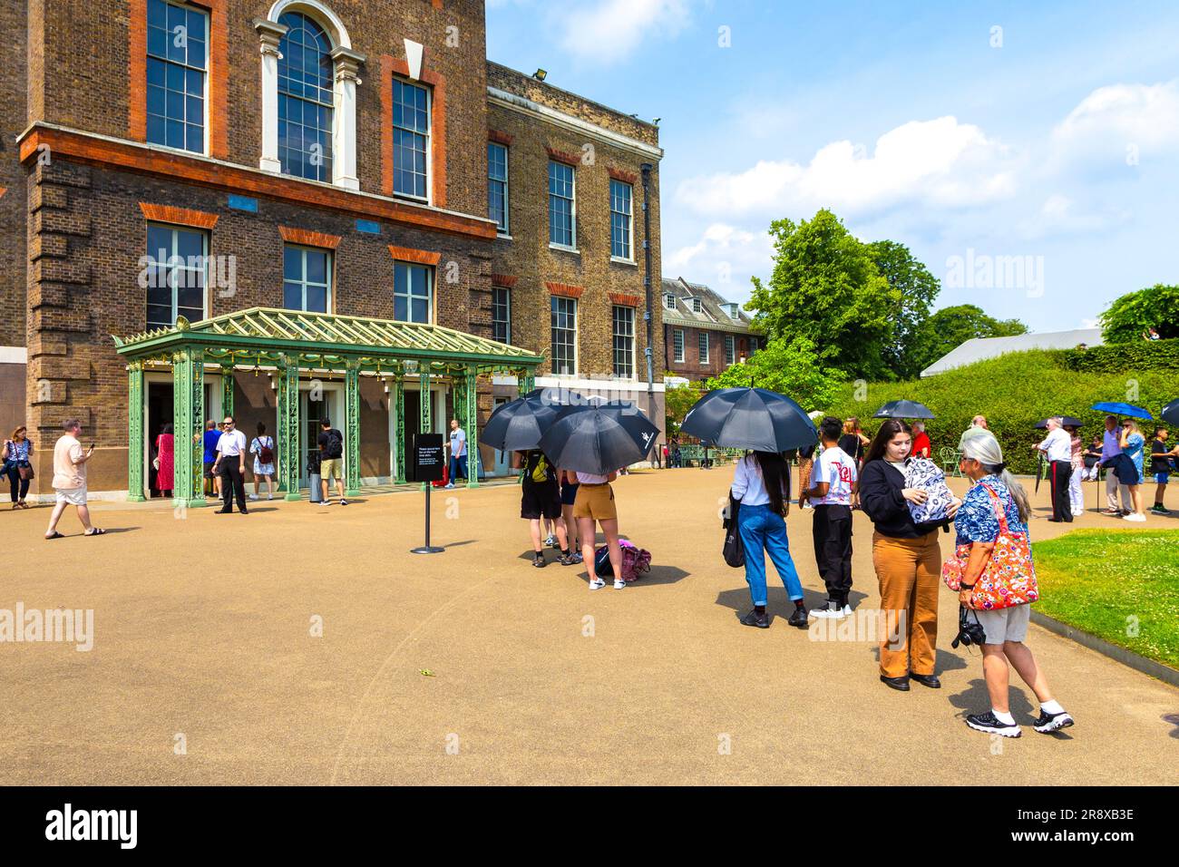 Touristen mit Sonnenschirmen an einem heißen Sommertag warten in der Schlange im Kensington Palace, London, England, Großbritannien Stockfoto