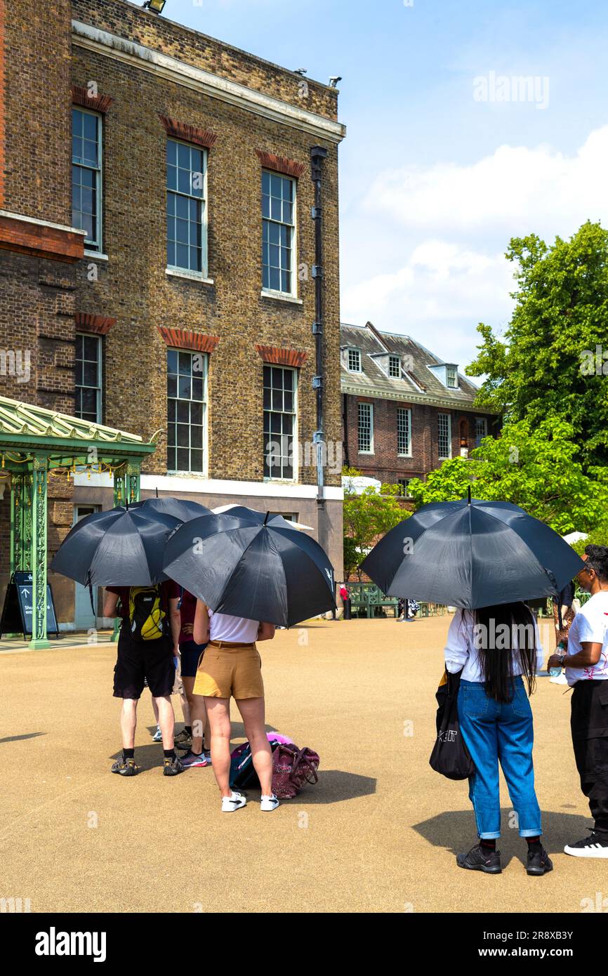 Touristen mit Sonnenschirmen an einem heißen Sommertag warten in der Schlange im Kensington Palace, London, England, Großbritannien Stockfoto