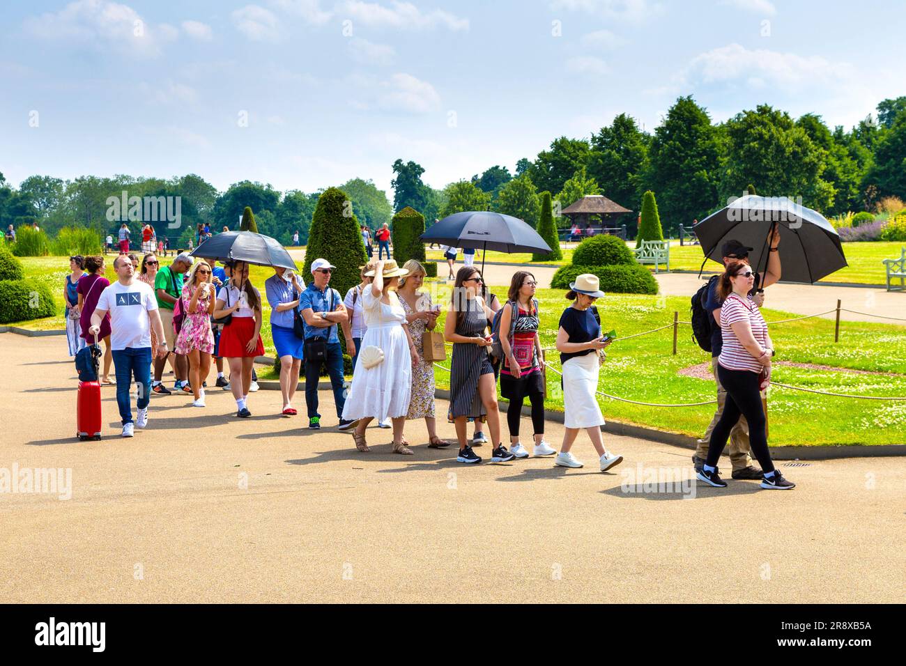 Touristen mit Sonnenschirmen an einem heißen Sommertag warten in der Schlange im Kensington Palace, London, England, Großbritannien Stockfoto