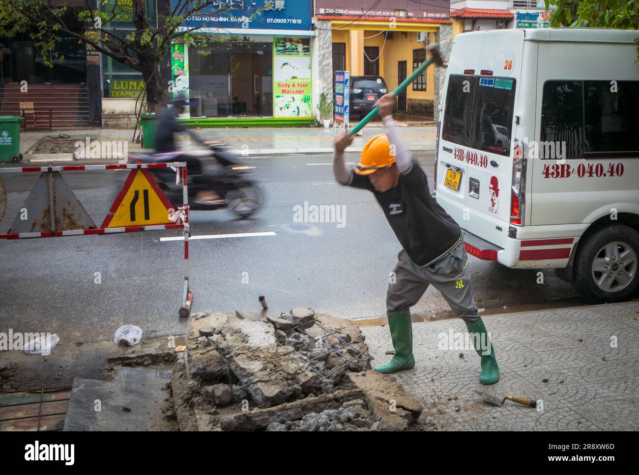 Ein Arbeiter zerschlägt Beton mit einem Vorschlaghammer auf dem Bürgersteig in Danang, Vietnam. Stockfoto
