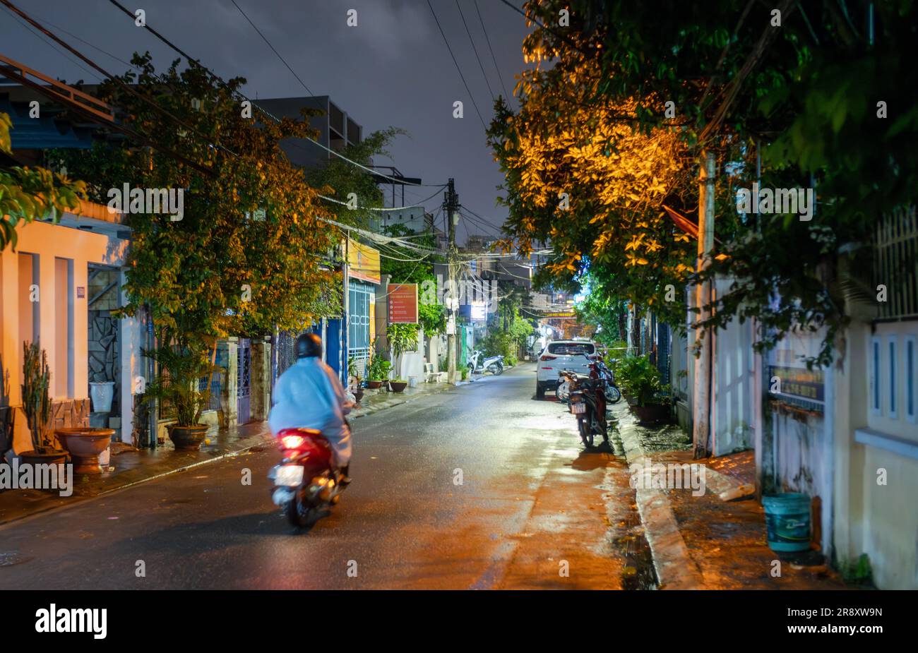 Ein Motorradfahrer fährt nachts eine kleine Straße im Regen in Danang, Vietnam. Stockfoto