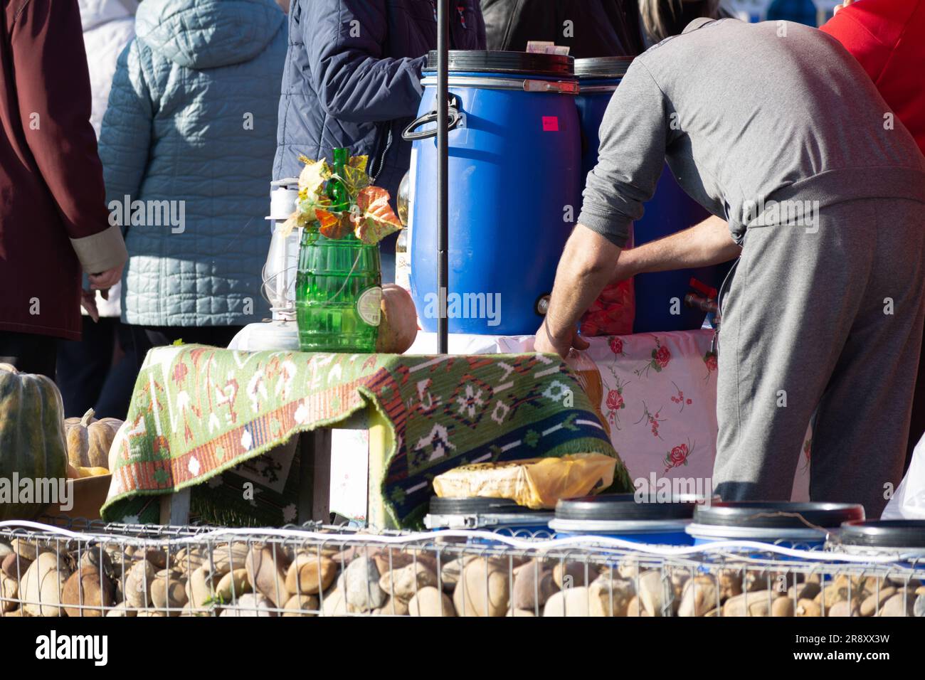 Ein Mann in einem grauen Trainingsanzug schüttet Weißwein in eine Plastikflasche in einem blauen Plastikfass. Weinfestival. Stockfoto