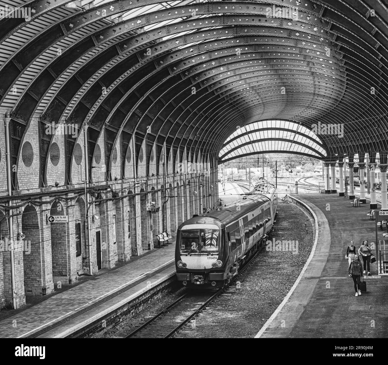 Ein Zug fährt unter einem historischen Eisendach aus dem 19. Jahrhundert von einem Bahnhof ab. Drei Passagiere verlassen eine Plattform mit Blick nach oben. Stockfoto
