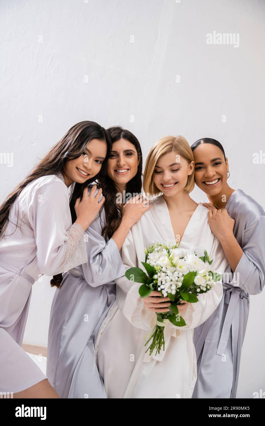 hochzeitsfeier, vier Frauen, fröhliche Braut mit einem Blumenstrauß in der Nähe von Brautjungfern in Seidenroben, kulturelle Vielfalt, Zusammengehörigkeit, Freundschaft Stockfoto