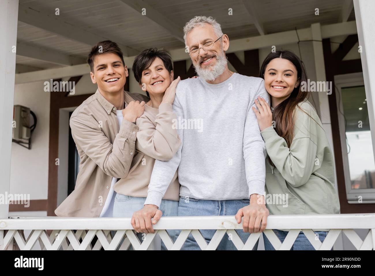 Elterntag Feier, Eltern mittleren Alters umarmen sich mit fröhlicher Tochter und Sohn auf der Veranda des Sommerhauses, schauen in die Kamera, Familientreffen, bondi Stockfoto