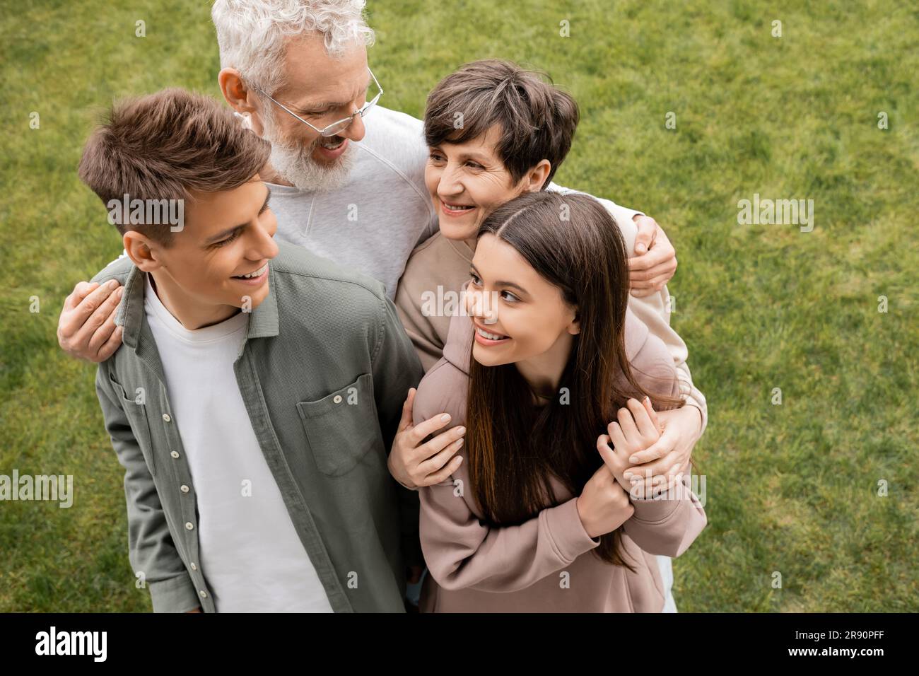 Blick von oben auf lächelnde Eltern mittleren Alters, die Kinder umarmen und sich anschauen, während sie den Elterntag im Juni im Garten feiern, Quality tim Stockfoto