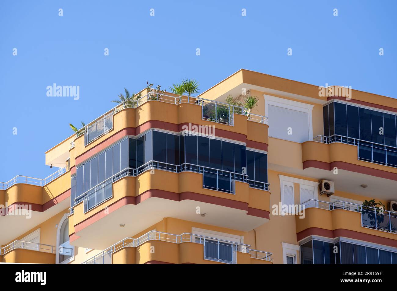 Großer verglaster Balkon, im obersten Stockwerk eines Wohnhauses. Ein Teil des Hauses gegen den blauen, klaren Himmel. Stockfoto