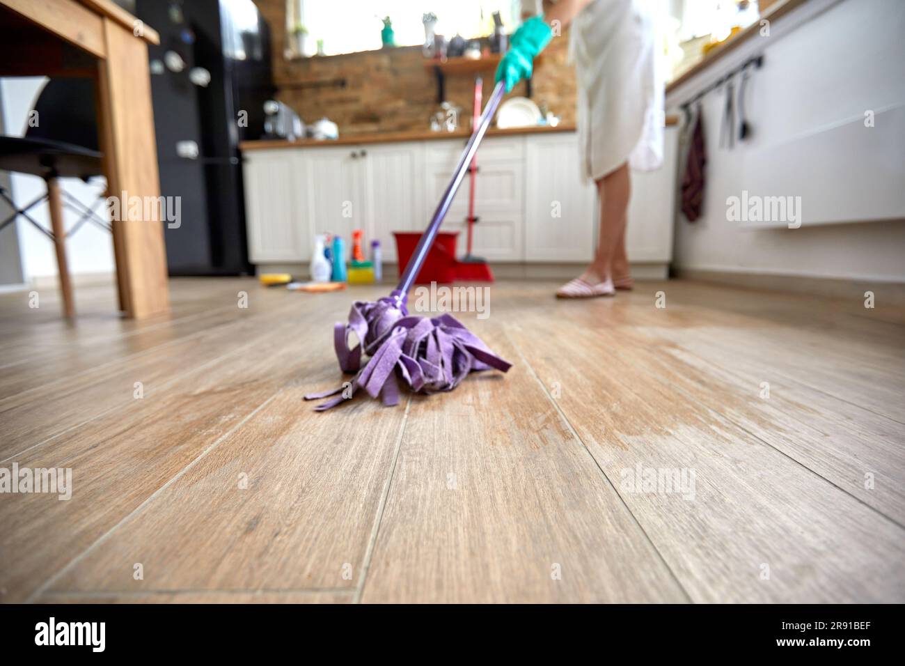 Die Frau kümmert sich um die Reinigung ihres Küchenbodens. Mit fachkundiger Präzision schwingt sie einen Mopp mit Finesse und gleitet ihn mühelos über die Oberfläche Stockfoto