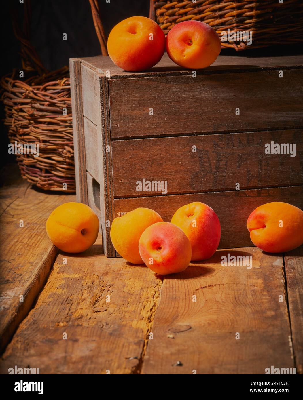 Frische lose Aprikosen, lose auf einer Holzkiste und einem Tisch mit einigen Körben im Hintergrund. Stockfoto