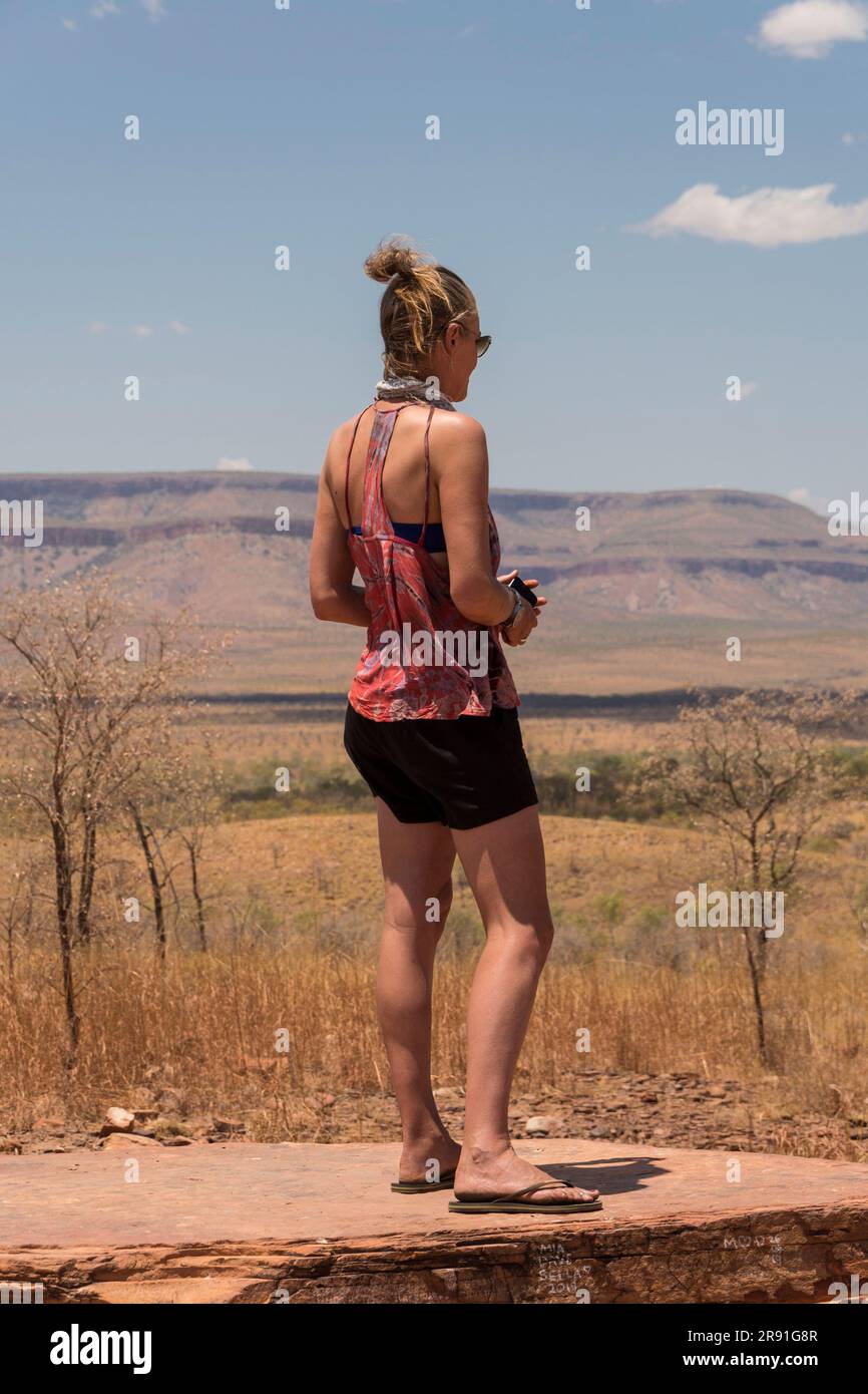 Eine Frau steht auf einem Felsentisch, um den Blick auf die Cockburn Ranges bei Durack in Westaustralien zu genießen Stockfoto