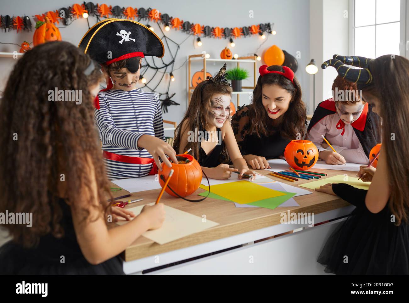 Junge Lehrerin mit ihren kleinen Schülern im Klassenzimmer, die sich auf Halloween vorbereiten. Stockfoto