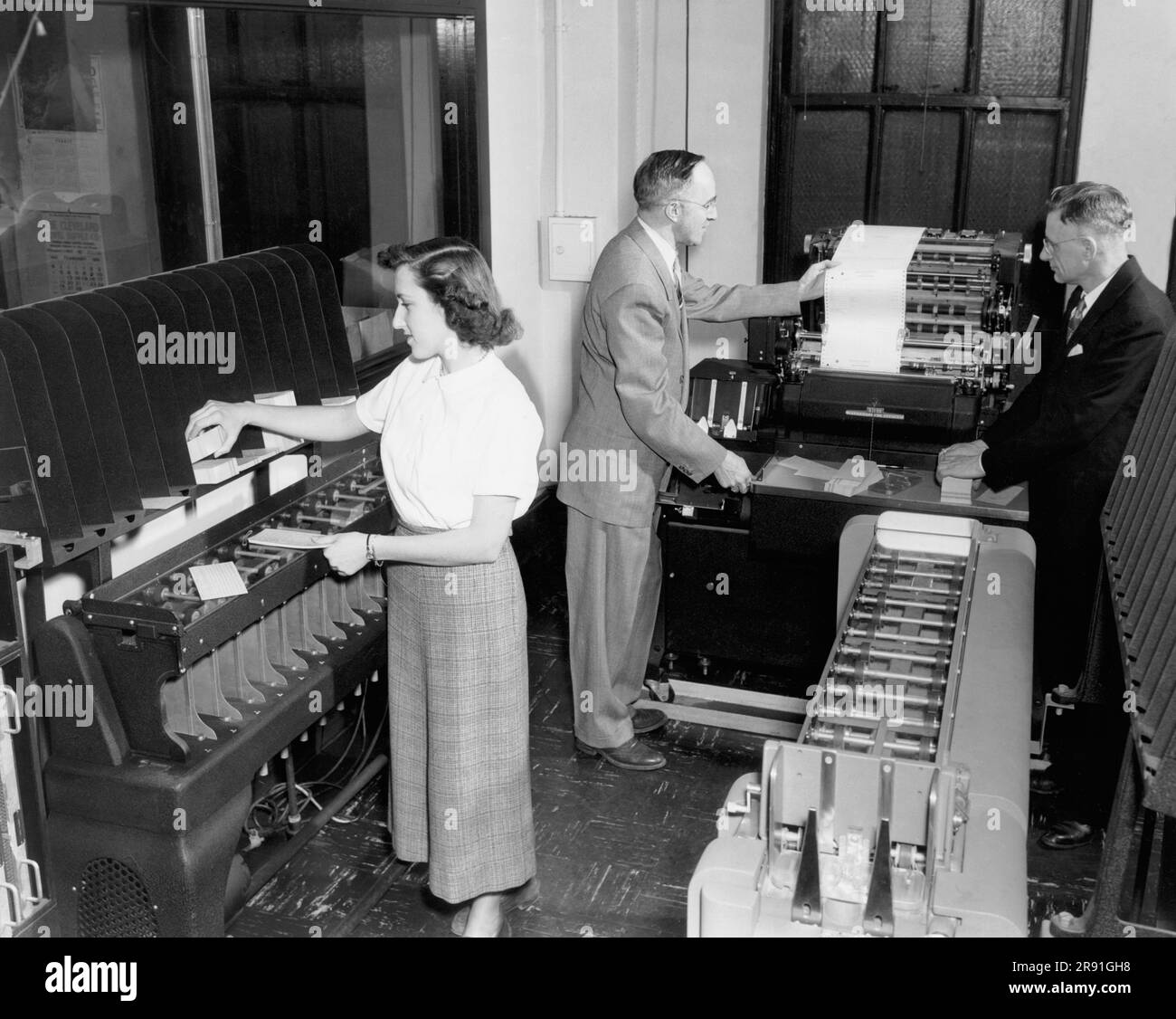 Cleveland, Ohio: Februar 1951, Eine Mitarbeiterin, die Lochkarten lädt, und zwei Männer, die sich einen Ausdruck von einem IBM-Buchhaltungsgerät in den Büros der Erie Railroad ansehen. Stockfoto
