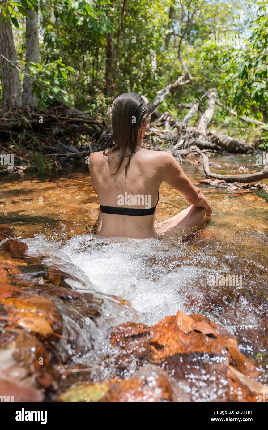 Eine Frau in einem Bikini hält sich in einem seichten Süßwasserstrom im Litchfield-Nationalpark in Australien kühl Stockfoto