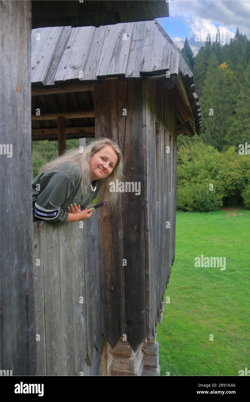 Das Foto wurde in den Karpaten in der Nähe der Kopie einer frei besuchten Festung gemacht. Das Bild zeigt ein Mädchen, das hinter dem Wald aus dem Haus guckt Stockfoto
