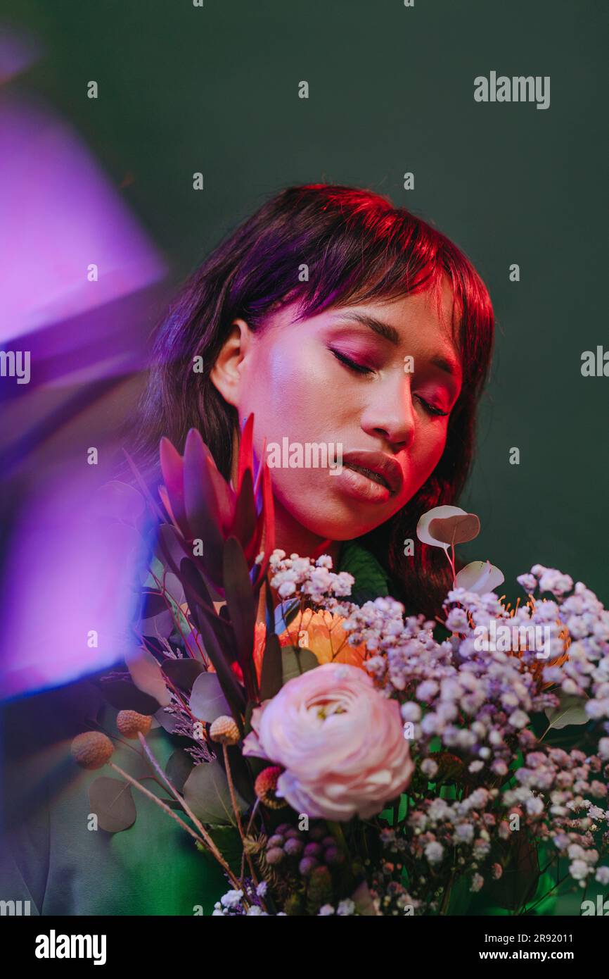 Frau inmitten von Neonlichtern und bunten Blumen vor grüner Kulisse Stockfoto