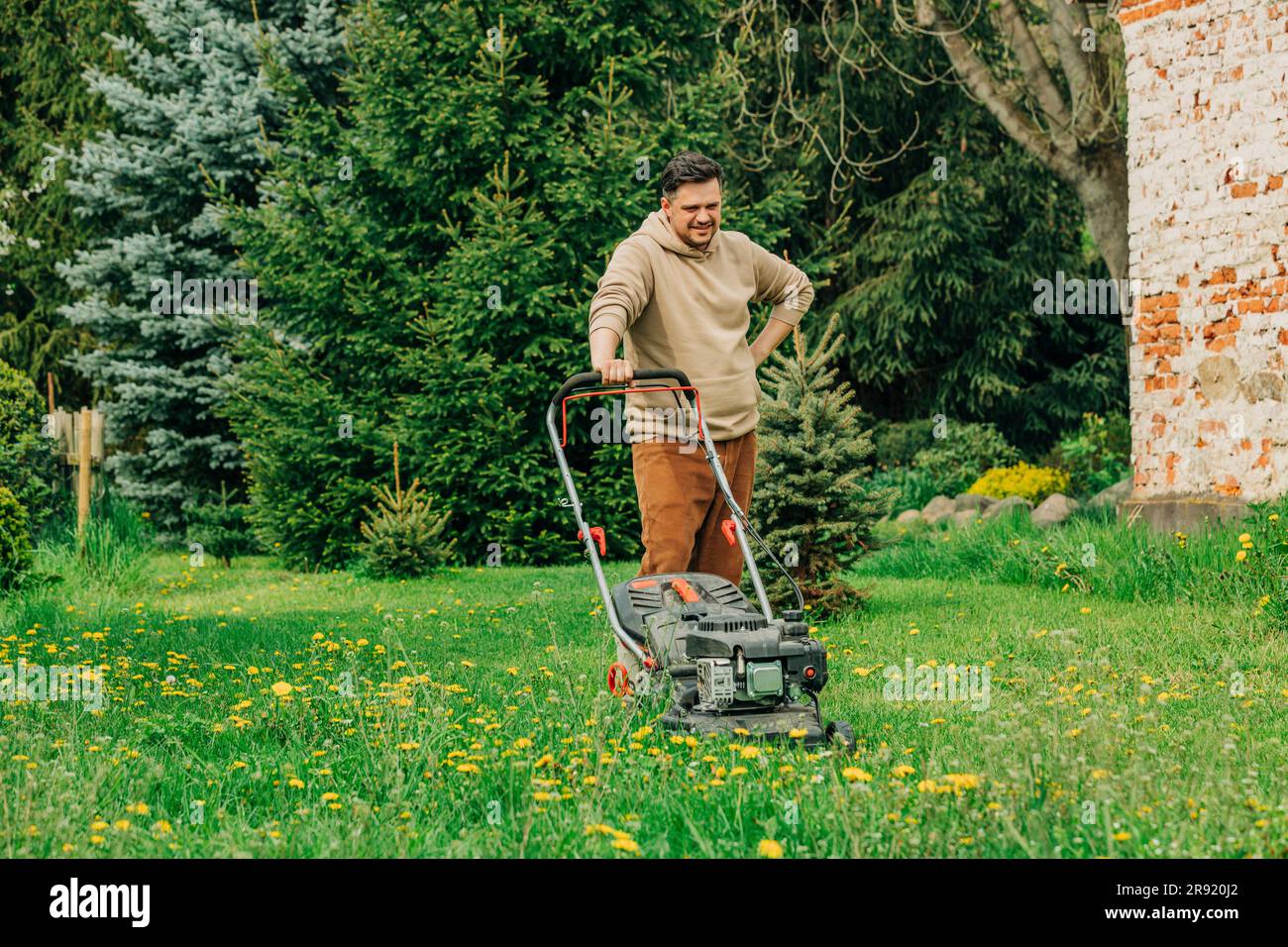 Mann, der Pause macht, steht mit Rasenmäher im Garten Stockfoto