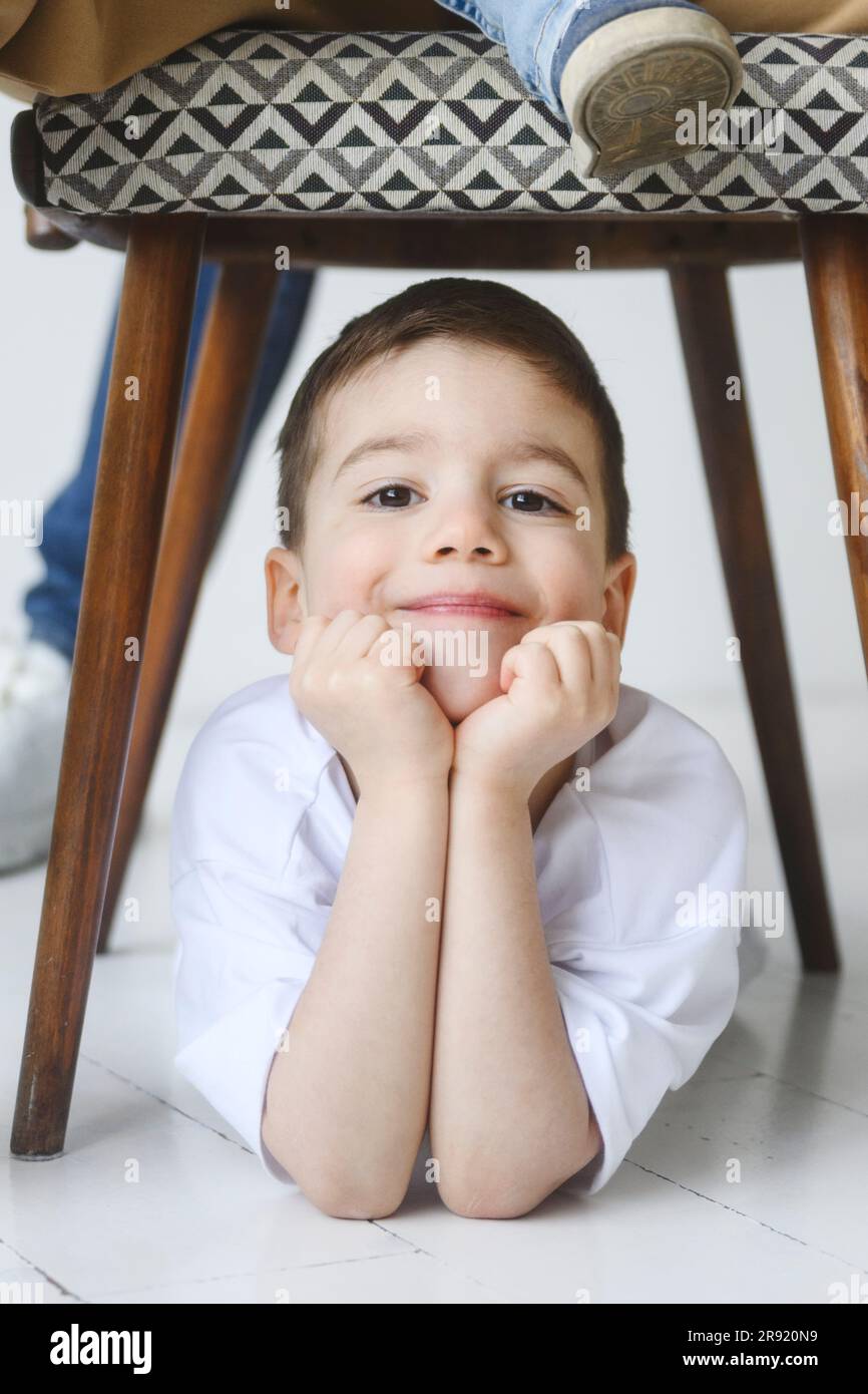 Lächelnder Junge, der sich unter dem Stuhl auf Ellbogen lehnt Stockfoto