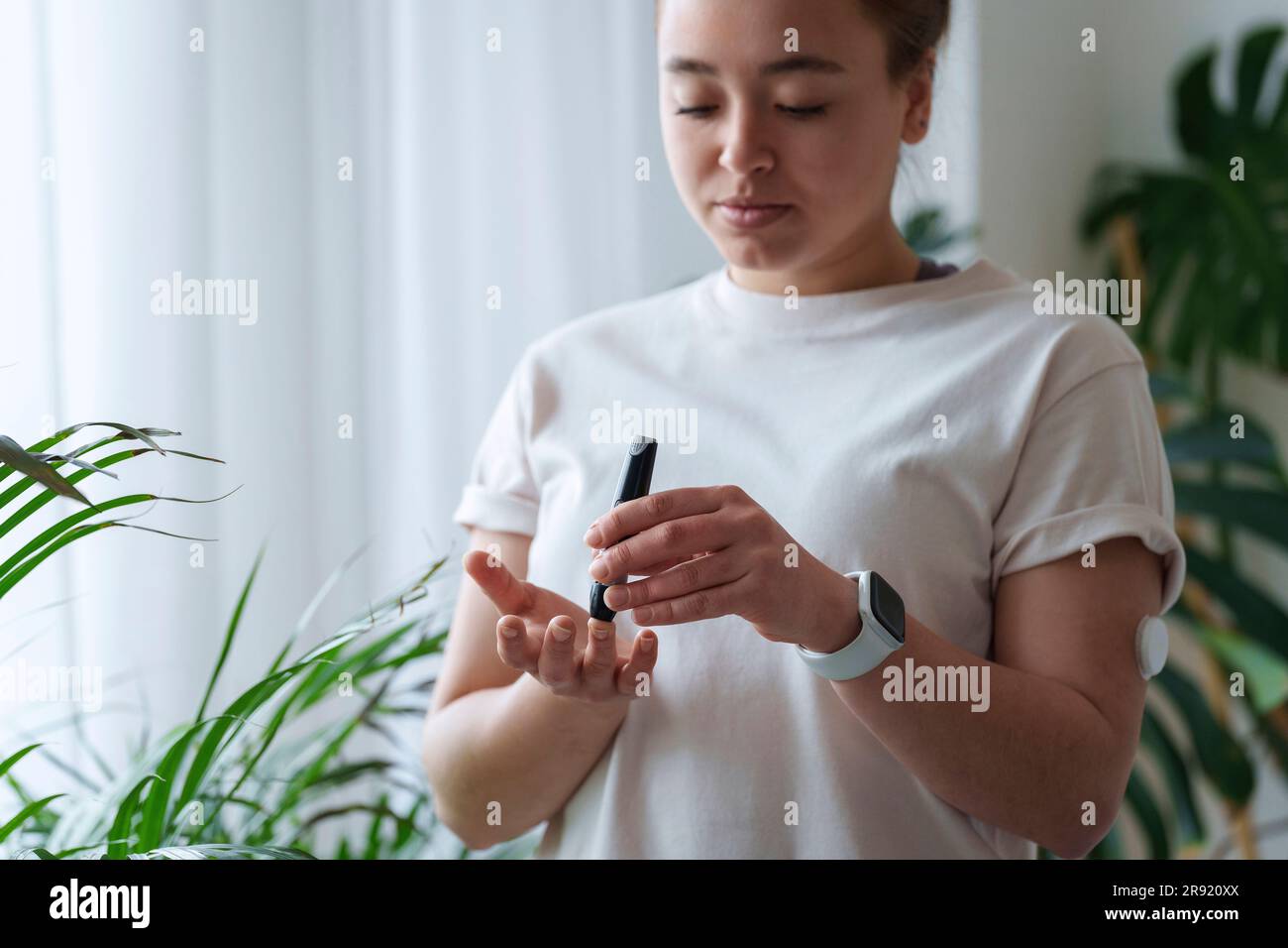 Eine Frau, die den Finger durchbohrt, um den Zuckergehalt zu Hause zu testen Stockfoto