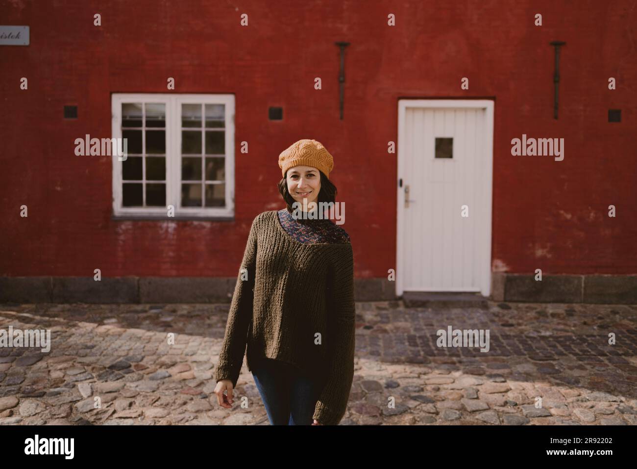 Eine Frau, die auf einer kopfsteingepflasterten Straße vor dem roten Gebäude steht Stockfoto