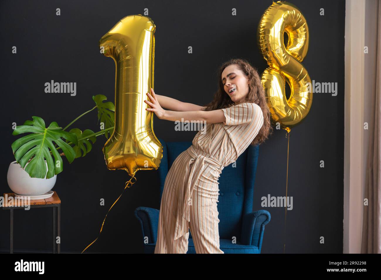 Verspielte junge Frau mit Heliumballon Nummer 1 zu Hause Stockfoto
